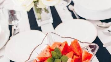 A dining table set with white plates, a glass bowl of watermelon salad, and a vase of white roses.