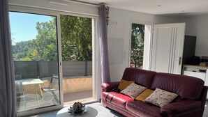 A living room with a red leather sofa, a small white table, and a glass door leading to an outdoor area.