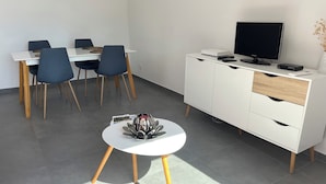 A modern dining area with a white table and blue chairs, a white cabinet with a TV, and a small white table with a decorative item.