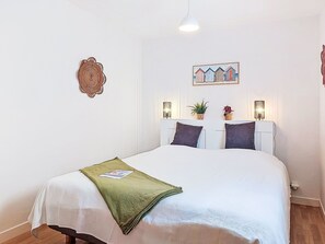 Un lit bien fait, agrémenté d’un plaid vert, deux lampes fixées au mur, un tableau encadré au-dessus du lit et un élément décoratif mural.