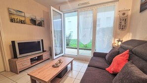 A living room with a TV, a wooden coffee table, a sofa, and a sliding glass door to a balcony. - L'air du Large by Interhome (Saint Malo)