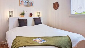 A bedroom with a bed, two bedside lamps, a wall-mounted picture, a window with a sailboat, and a potted plant. - L'air du Large by Interhome (Saint Malo)
