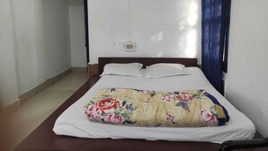 Ein Schlafzimmer mit Bett, weißen Wänden, einem Fenster mit blauen Vorhängen und einer sichtbaren Steckdose an der Wand.