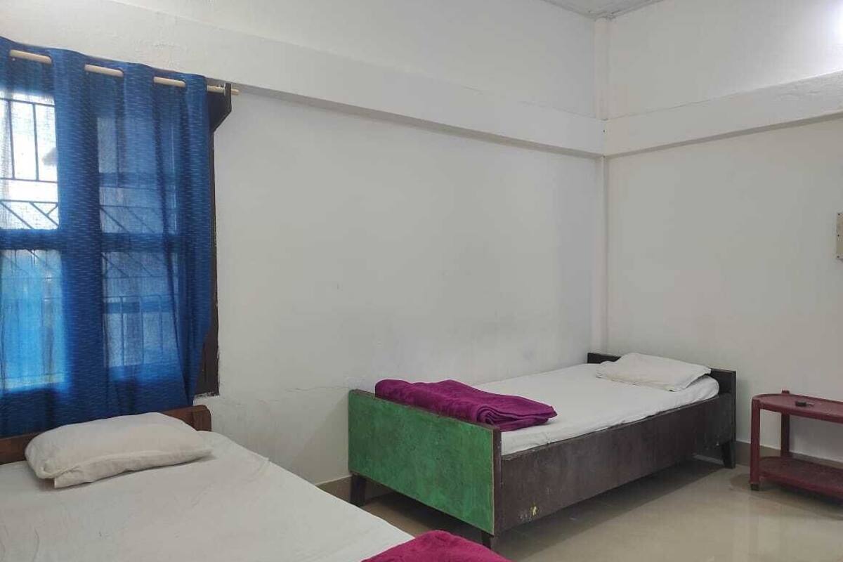 A room with two single beds, a small table, and a window with blue curtains.