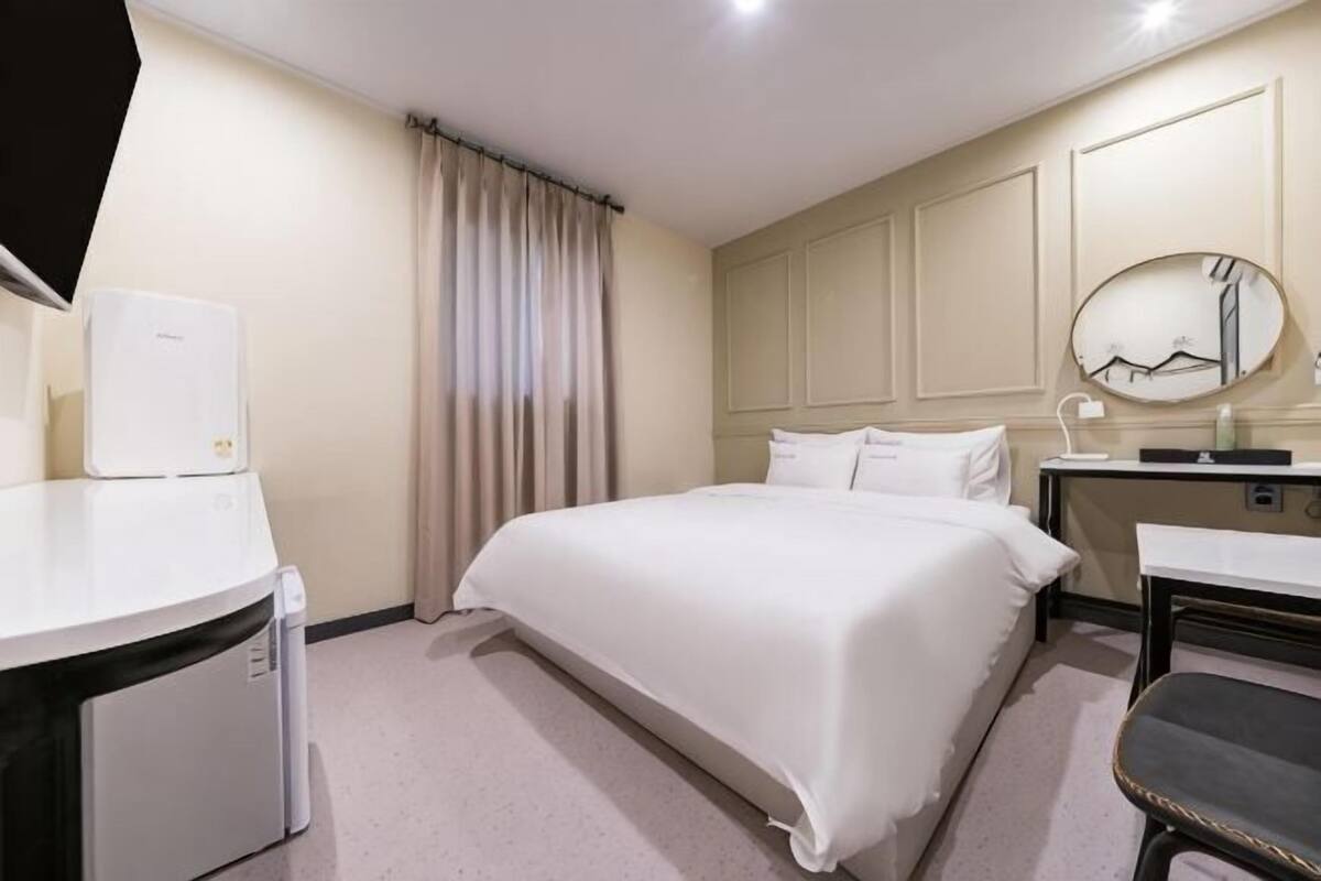Ein Hotelzimmer mit Bett, Schreibtisch, Stuhl, Spiegel und einem Fenster mit Vorhängen.