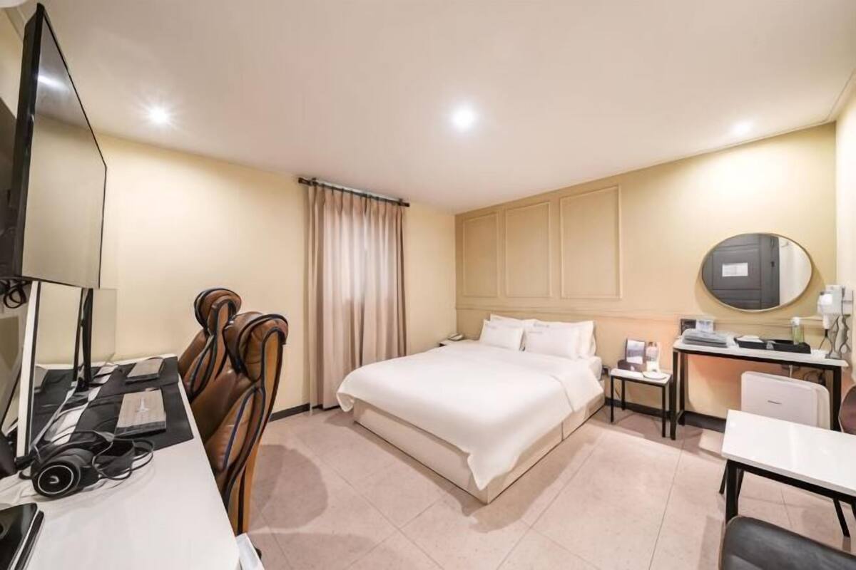 Ein Hotelzimmer mit Bett, Schreibtisch, Stuhl, Fernseher und Spiegel.