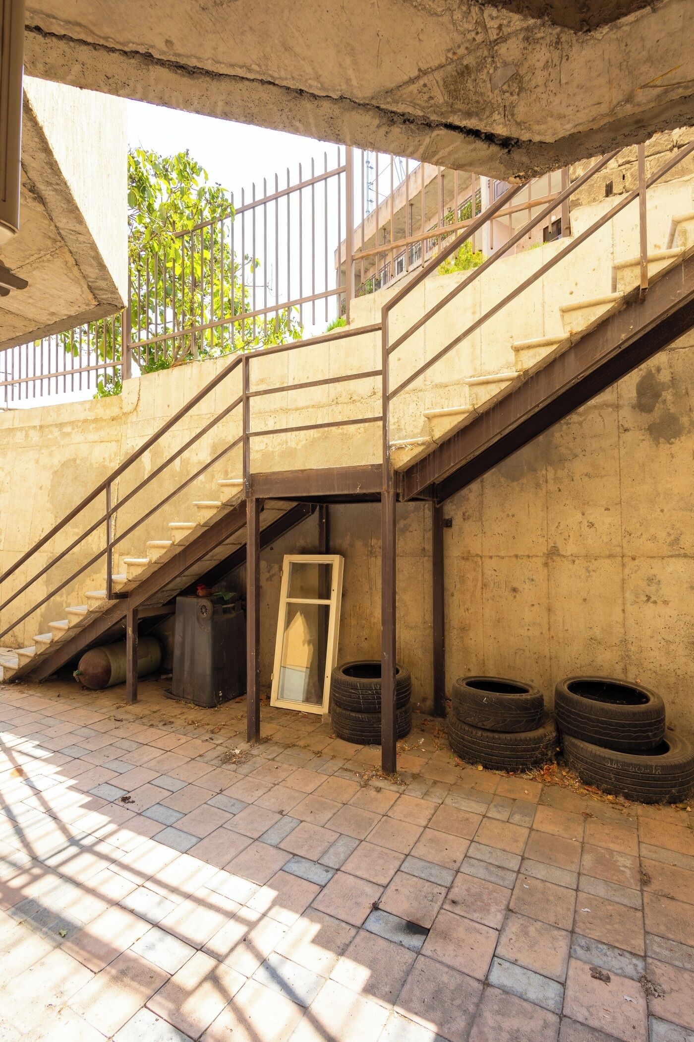 Uma escadaria de concreto com grades de metal, uma porta e vários pneus descartados.