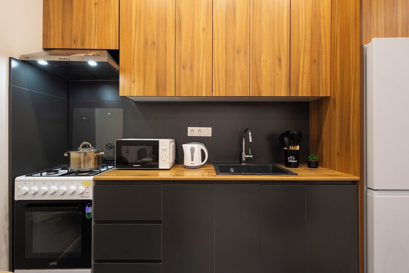 A compact kitchen with a gas stove, a microwave, a kettle, and a sink.