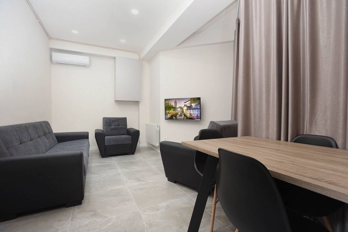 Une pièce moderne avec une table en bois, des chaises noires, un canapé gris et un fauteuil gris.