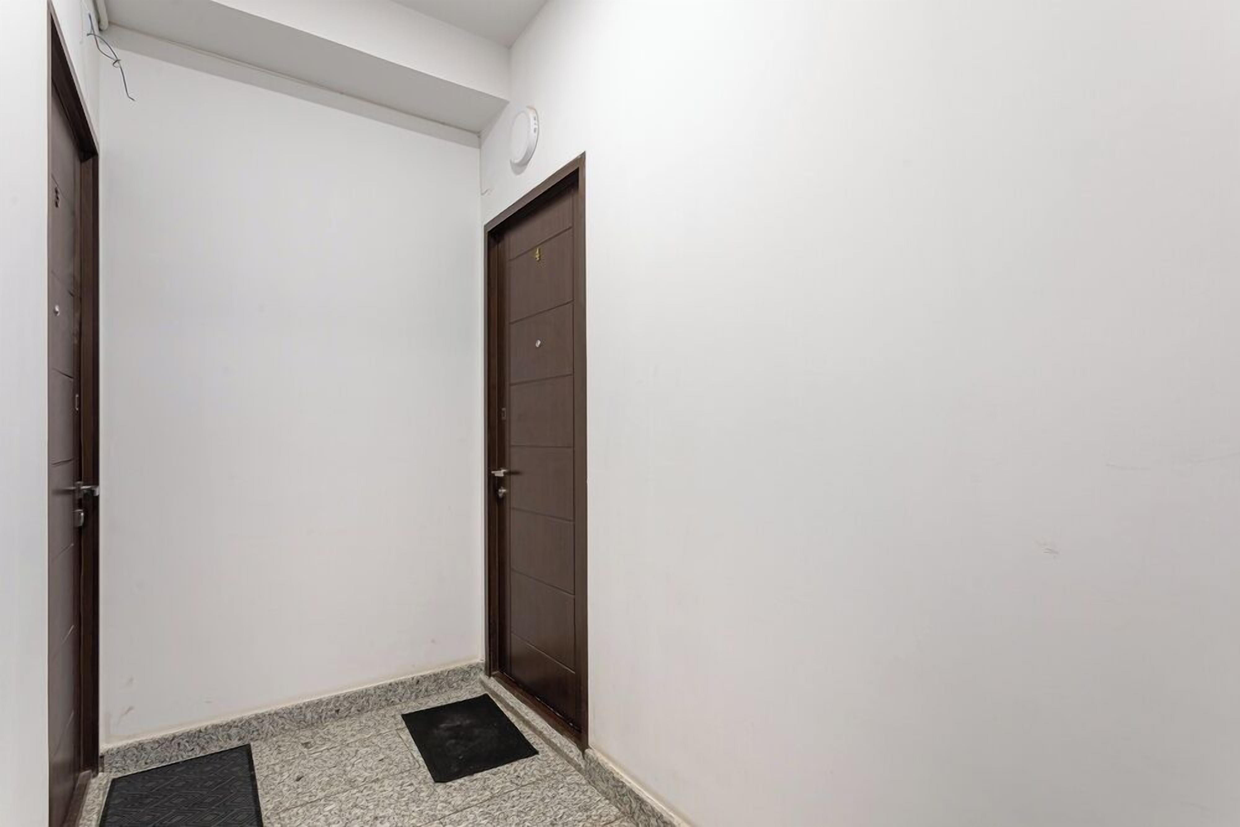 Um corredor estreito com uma porta marrom escura e uma parede branca.