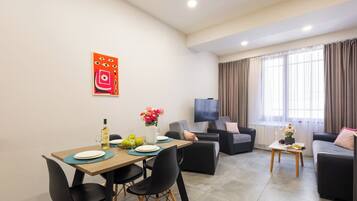 A modern living room with a dining area, a flat-screen TV, and a large window with curtains.