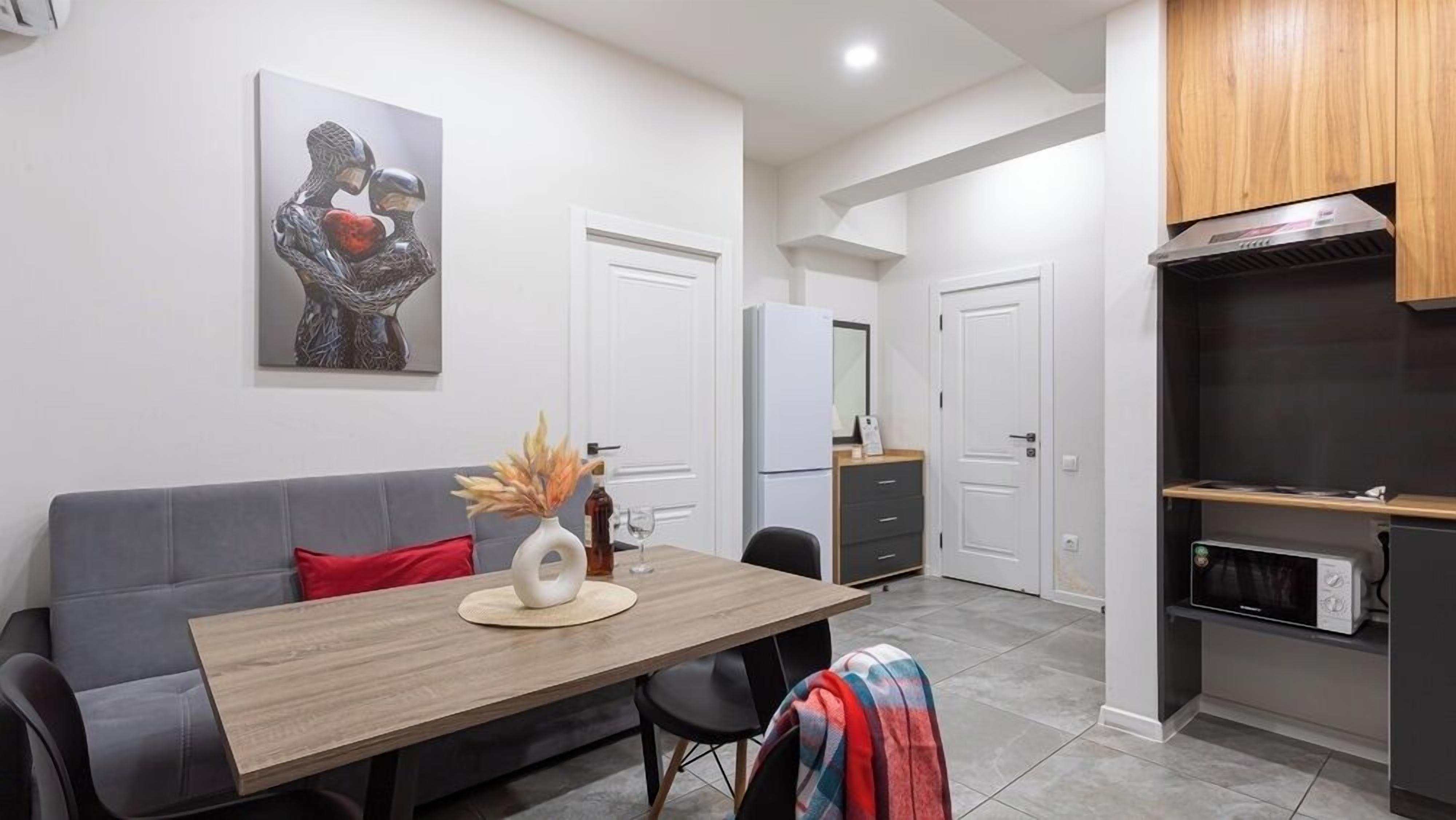 A modern kitchen with a dining area, featuring a grey sofa, a wooden dining table, and a microwave.