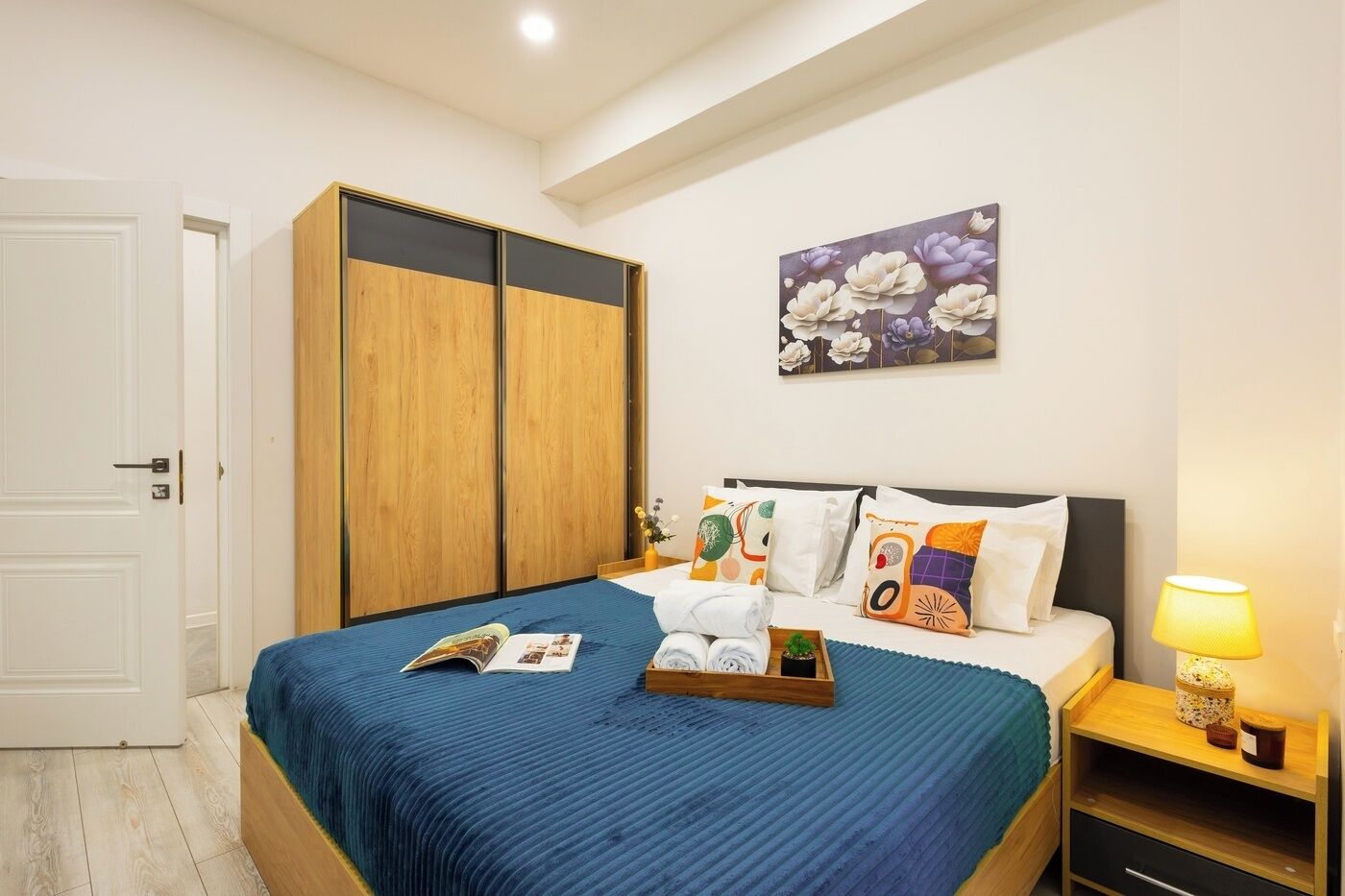 Un dormitorio con cama, armario, mesita de noche con lámpara y una obra de arte floral en la pared.