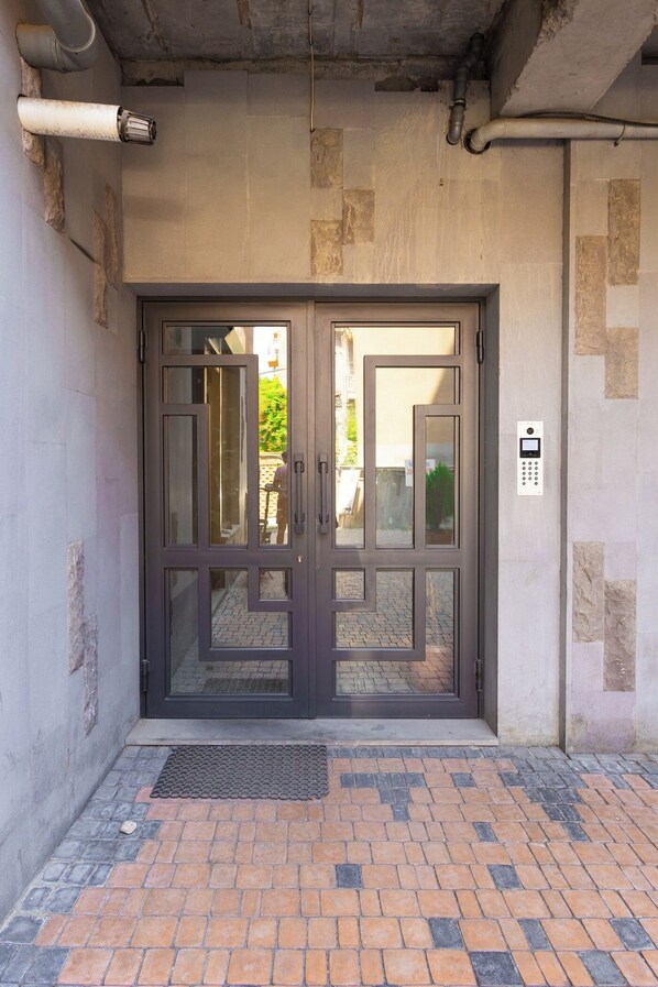 A double door entrance with a keypad lock, a doormat, and a small outdoor area with a tiled floor.