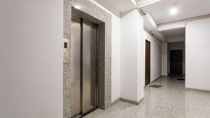 A hallway with a marble floor, a door with a digital display, and a light fixture on the ceiling. - Stay Inn on Saryan 26.3 str. (Yerevan)