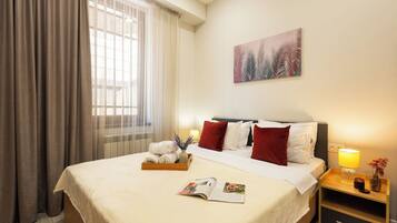 Habitación de hotel con una cama, una mesita de noche con lámpara, una ventana con cortinas y un cuadro en la pared.