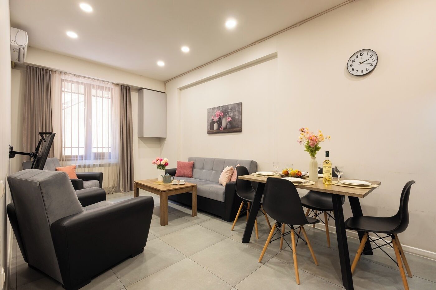 A modern living room with a sofa, chairs, a dining table, and a clock on the wall.