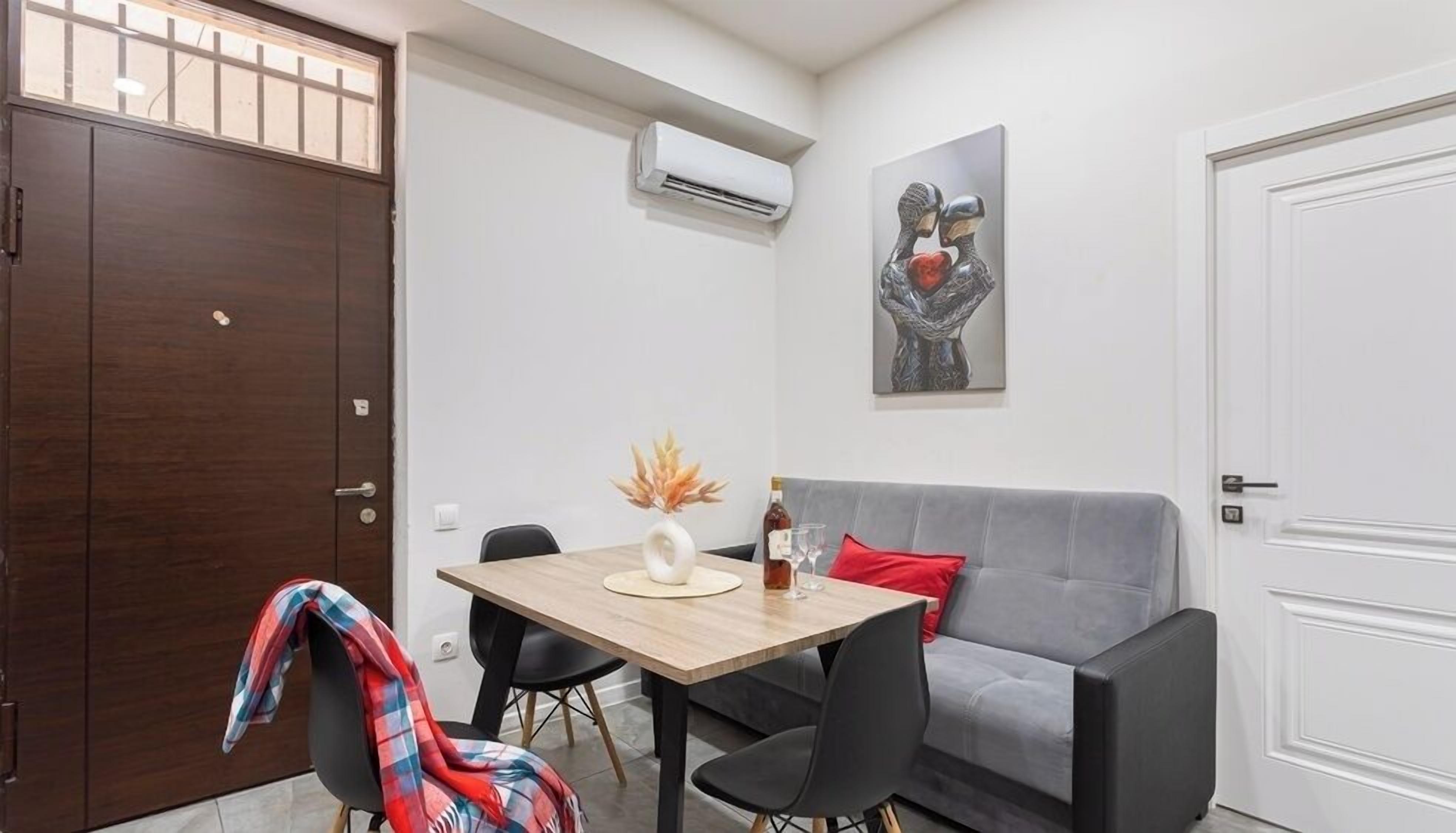 A dining area with a table, chairs, a sofa, and an air conditioning unit.