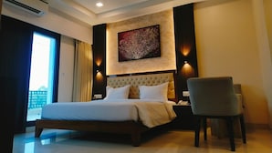 Een moderne hotelkamer met een groot bed, een plafondventilator, een airconditioning en een kunstwerk aan de muur, plus een stoel.