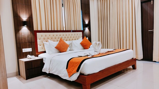 Een net opgemaakt bed met wit en oranje beddengoed, een houten hoofdbord en een nachtkastje met een telefoon.