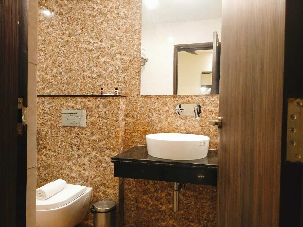 A bathroom with a marble wall, a white sink, a mirror, and a toilet.