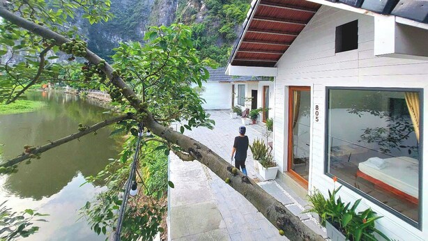 A modern building with a large glass window, a stone pathway, and a view of a lake and mountains. - Vivian riverside cottage - Ninh Bình (Ninh Binh)