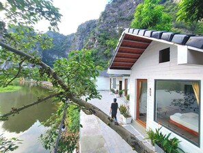 A modern building with a large window, a balcony, and a view of a river and mountains. - Vivian riverside cottage - Ninh Bình (Hoa Lu)