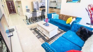 A modern living room with a blue sofa, a coffee table, and a dining area with chairs and a table. - Lux Suites Urban Oasis Apartments (Nairobi)