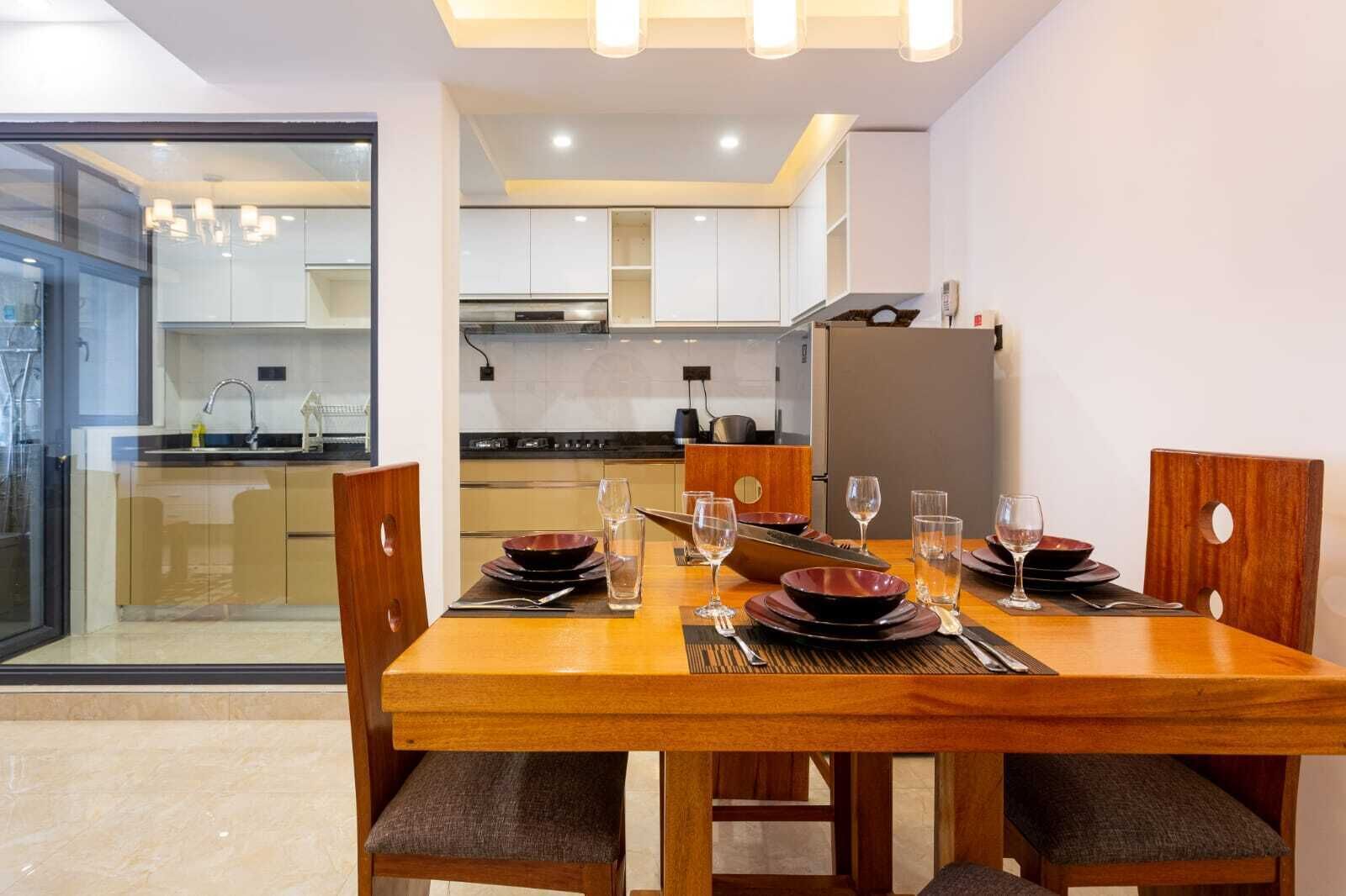 A modern dining area with a wooden table set for four, equipped with plates, bowls, glasses, and cutlery.