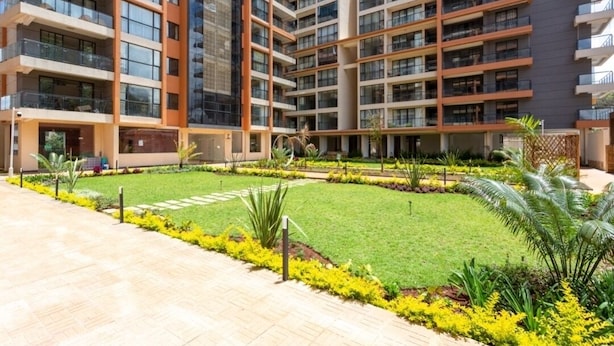 A modern multi-story residential building with balconies, a central courtyard with grass and plants, and a paved walkway. - Lux Suites Urban Oasis Apartments (Nairobi)