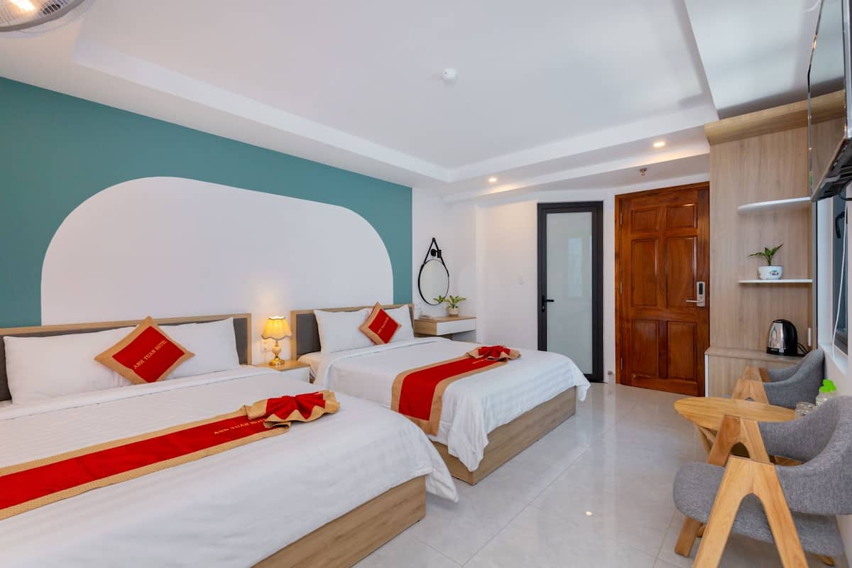 Habitación de hotel con dos camas, una puerta de madera, una mesita con sillas y una ventana.