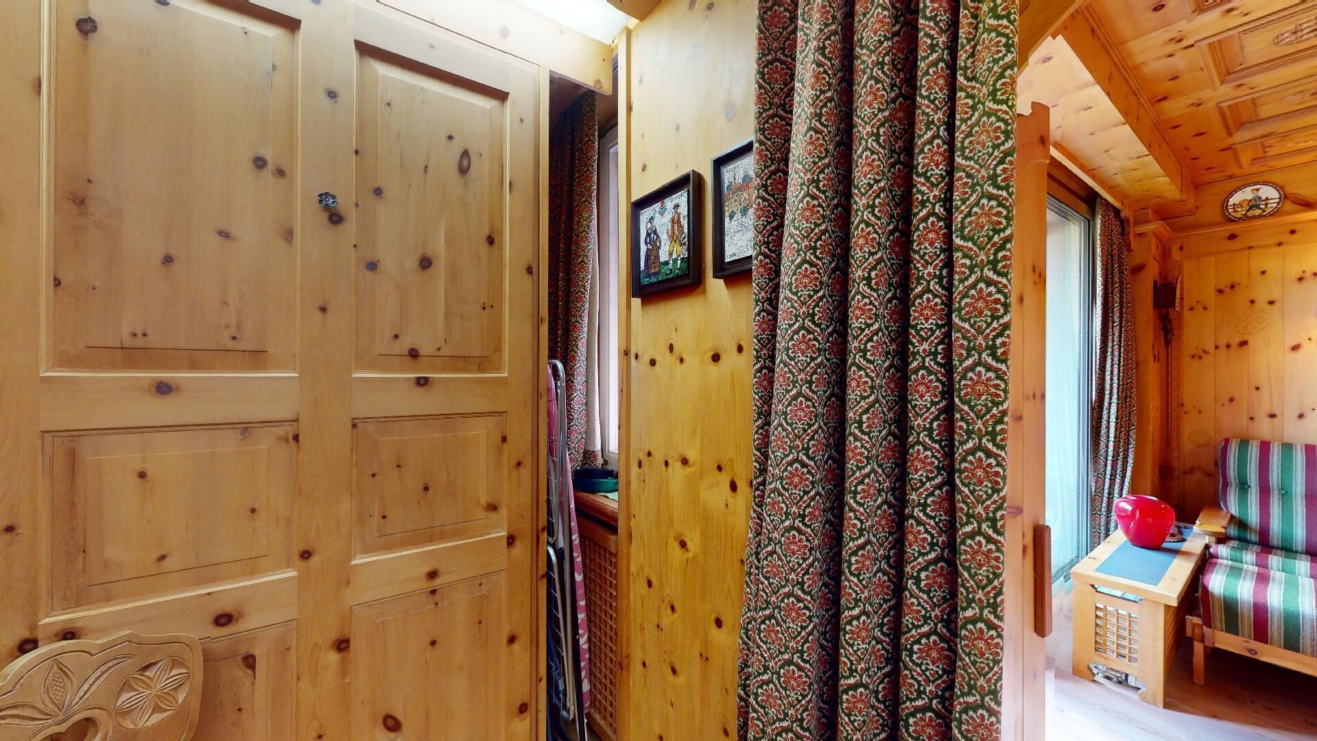 A wooden interior with a patterned curtain, a wooden bench, and a small table with a red object on it.