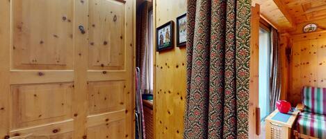 A wooden interior with a patterned curtain, a wooden bench, and a small table with a red object on it.