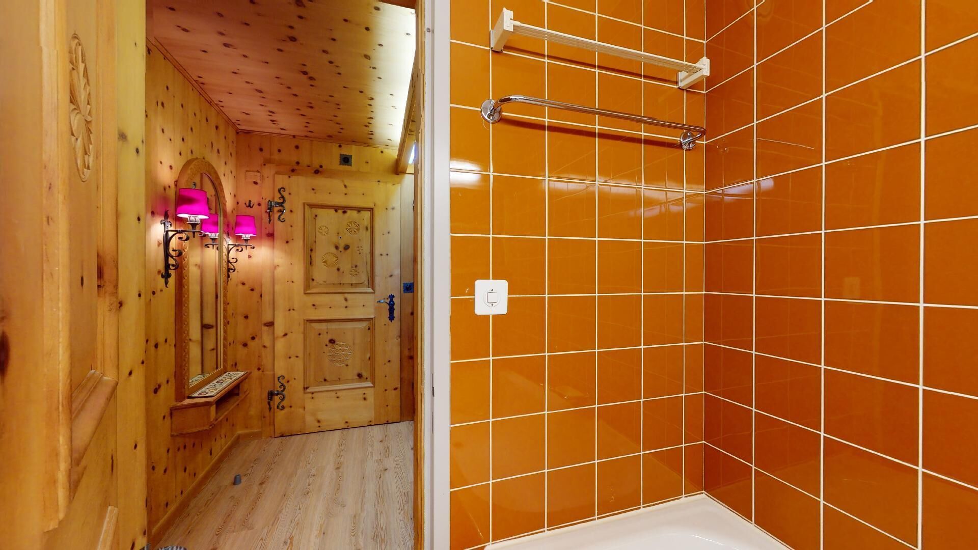 Ein Badezimmer mit Holzwänden, einer gefliesten Duschkabine und einer Holztür mit Verzierungen.