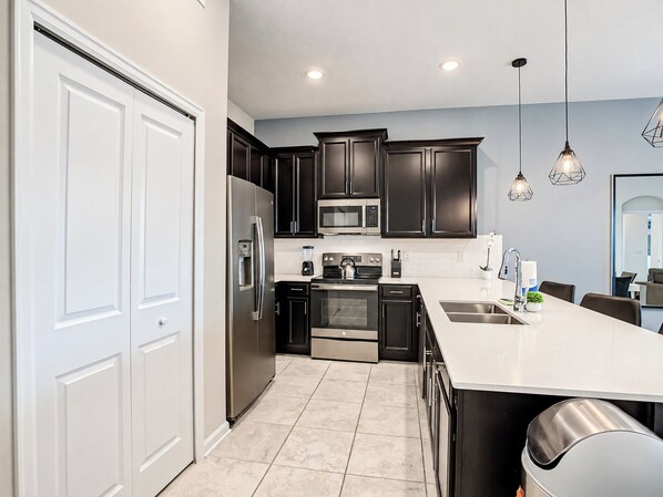 A modern kitchen with stainless steel appliances, dark cabinetry, and a white countertop.