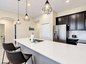 A modern kitchen with a large island, black cabinets, and pendant lighting. - Cozy Hideaway/Waterpark/GameRoom (Davenport)