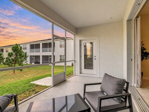 A balcony with a view of a building and a tree, a door, and a chair.