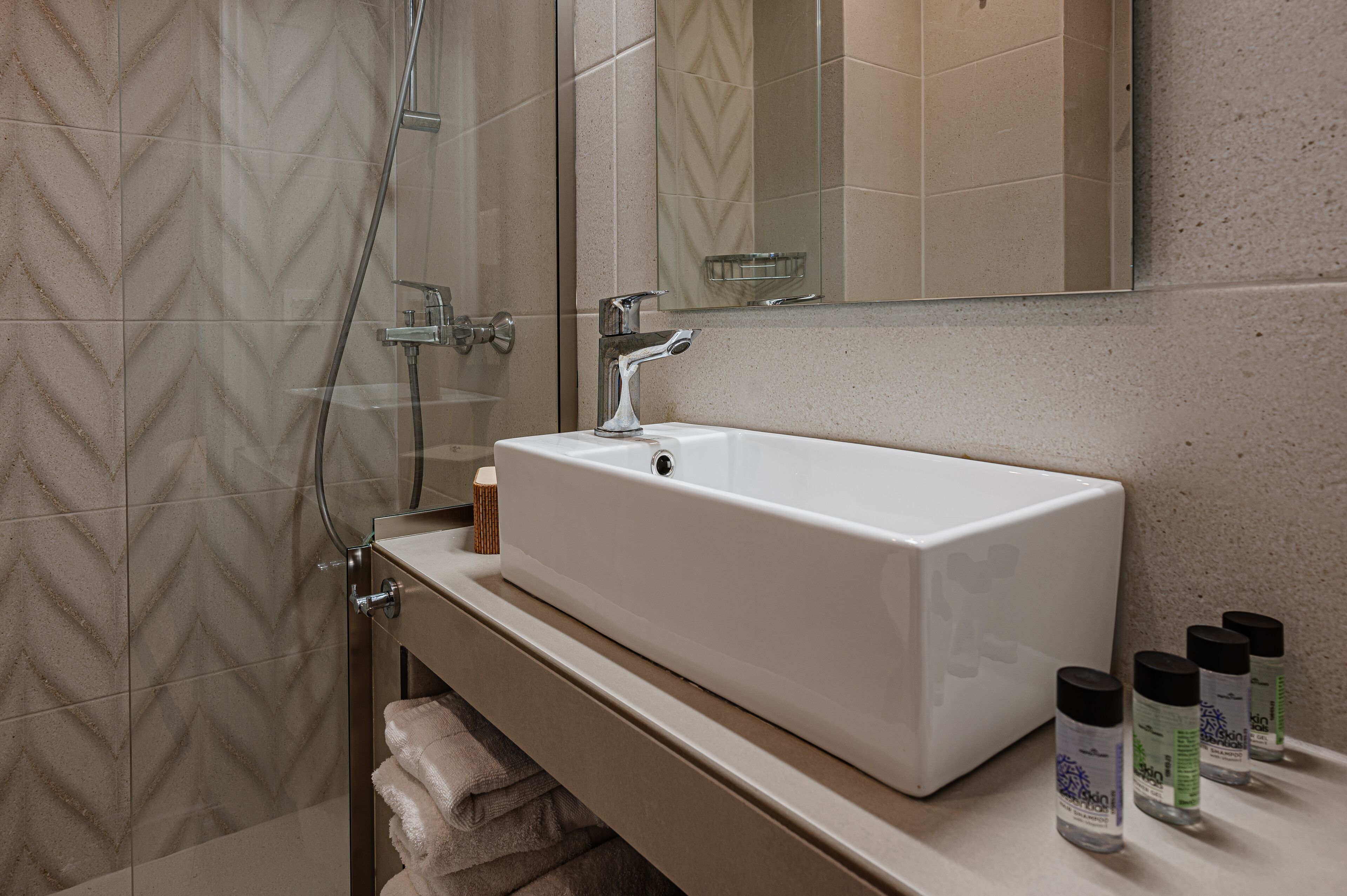 Un baño con un lavabo rectangular, una cabina de ducha de vidrio y un espejo sobre el lavabo.