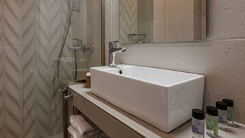 Un baño con un lavabo rectangular, una cabina de ducha de vidrio y un espejo sobre el lavabo.
