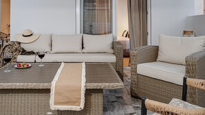 A modern living room with a sofa, two armchairs, a coffee table, and a dining table with wine glasses and a plate of strawberries.