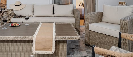 A modern living room with a sofa, two armchairs, a coffee table, and a dining table with wine glasses and a plate of strawberries.