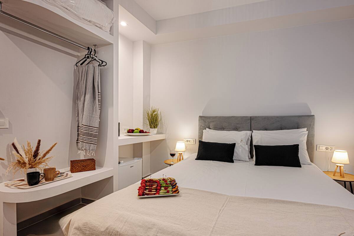 Quarto de hotel moderno com uma cama grande, mesas de cabeceira, uma pequena escrivaninha e um porta-toalhas.