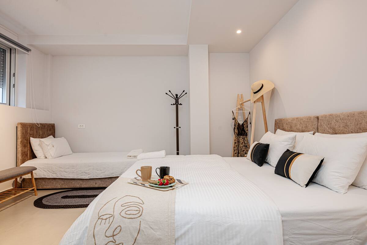 Quarto de hotel moderno com duas camas, um cabideiro, um banco e uma bandeja de café da manhã sobre a cama.