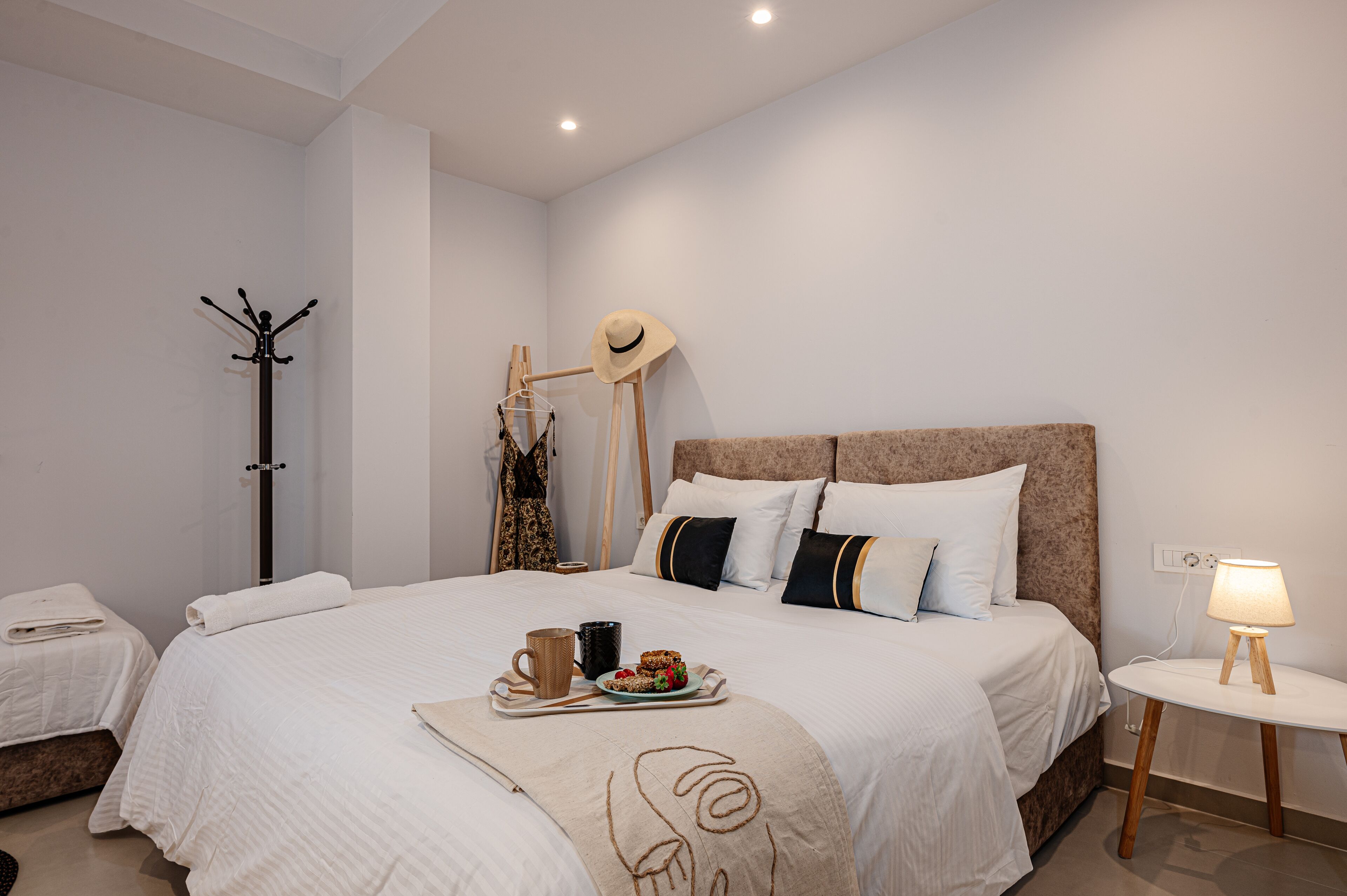 A bedroom with a large bed, a bedside table with a lamp, a coat rack, and a hanging hat.