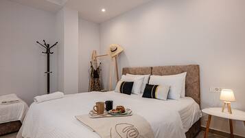 A bedroom with a large bed, a bedside table with a lamp, a coat rack, and a hanging hat.
