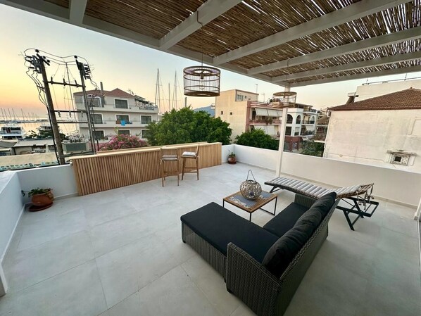 A rooftop terrace with a sofa, chairs, and a table, overlooking a marina and buildings.