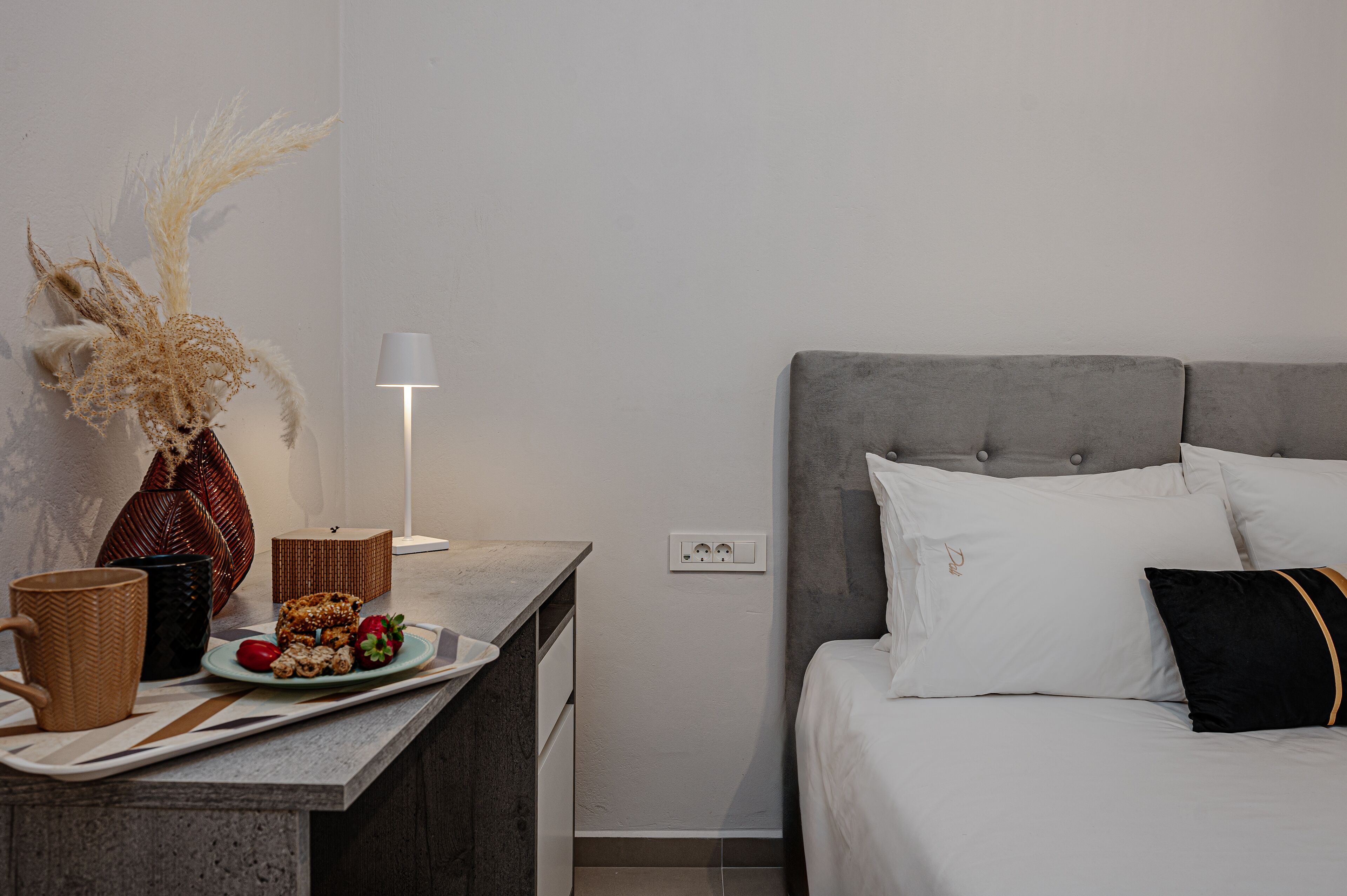 Un dormitorio ordenado con cama, mesita de noche, lámpara y elementos decorativos.