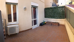 A small courtyard with a tiled floor, a window, a wall-mounted light, and a green hedge. - Vacation Home Paradise (Viterbo)