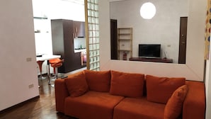 A living room with a sofa, a television, and a kitchen in the background. - Vacation Home Paradise (Viterbo)