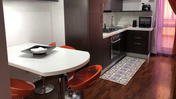 A compact kitchen with a white countertop, dark cabinets, a microwave, and a gas stove. There are two red chairs around a small table with a tray. - Vacation Home Paradise (Viterbo)